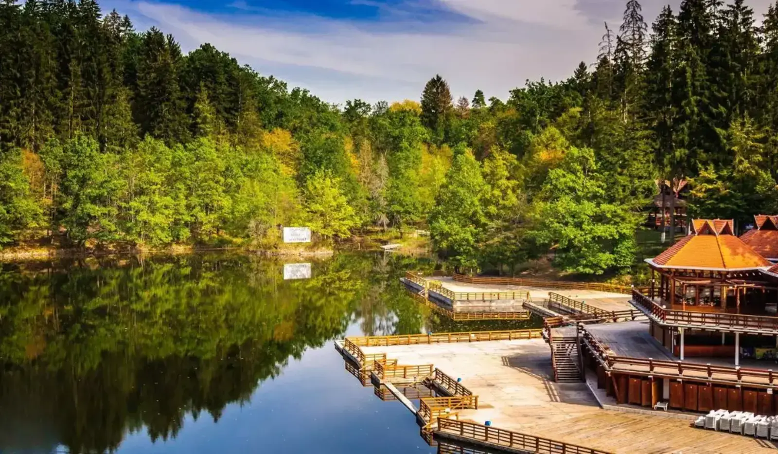 Lacul Ursu din Sovata, cu ponton pe mal și pădure de conifere &icirc;n fundal, reflexii &icirc;n apă.
